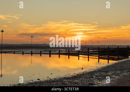 Southend on Sea, UK. 6th Oct, 2025. A tranquil coastal scene at sunset, featuring wooden groynes and navigation markers extending into calm waters. The sky glows with warm hues of orange and pink, reflecting on the wet sand and pebbled shoreline. A peaceful moment capturing the harmony between natural beauty and maritime infrastructure. Sunsets on the River Thames Estuary at the beach in Southend on Sea. Penelope Barritt/Alamy Live News Stock Photo