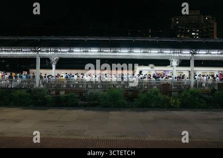 Mumbai, India - 23 September 2025: View of a bustling train station platform under bright lights as a train blurs past the crowd, capturing the energy of Mumbai's transport. Stock Photo