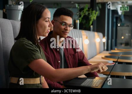 Diverse young colleagues in smart casuals discussing over laptop at desk in office Stock Photo