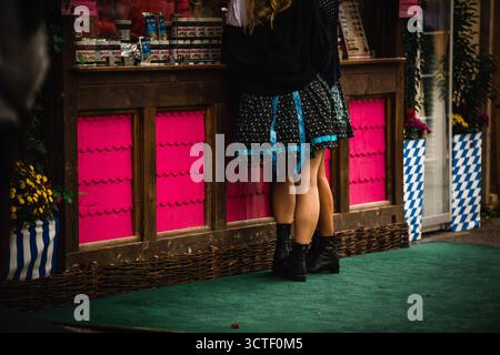 Munich, Germany - 18 September 2022: View of a vibrant pink stall front at Oktoberfest, where a couple stands closely, their legs a study in contrast against the green carpeted ground. Stock Photo
