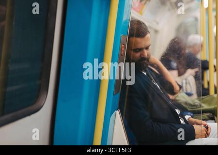 Side view of man napping in subway train, travelling from work. Stock Photo