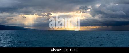 Dramatic horizon on Geneva lake with sun rays breaking through dark clouds. Stock Photo