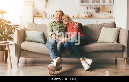 Happy Mature Couple Embracing Posing Sitting On Couch At Home Stock Photo