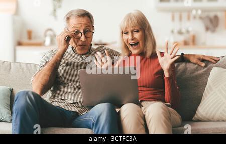 Emotional Mature Couple Using Laptop Computer Shouting In Excitement Indoor Stock Photo