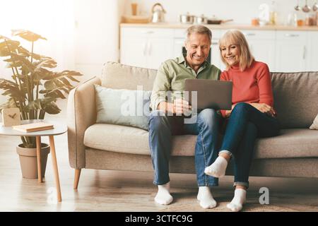 Cheerful Senior Spouses Using Laptop Watching Movie Onilne At Home Stock Photo