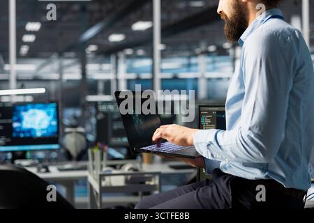 Programmer coding in high tech data center office, updating AI automation scripts. Server room employee programming artificial intelligence algorithms, debugging equipment racks Stock Photo