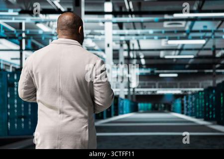 Technician walking in server room, overseeing mainframes gear used for managing databases. IT expert in data center workplace doing checkup on rackmounts storing information Stock Photo
