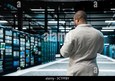 Admin in data center updating systems using tablet, conducting security audits to protect against cyber threats. Server hub IT specialist using device, deploying cybersecurity measures Stock Photo