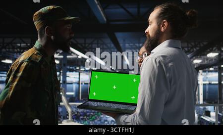 Army engineering team in command center server hub using mockup laptop to install and maintain IT systems. Military data center admins overseeing information systems with chroma key notebook, Stock Photo