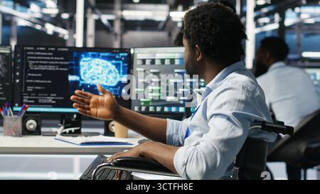 Man in wheelchair dissatisfied with server farm AI analytics metrics. Data center admin with paraplegia frustrated by glitches while automating tasks using node tree programming tool, camera B Stock Photo