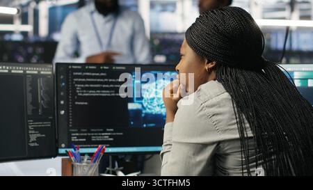 Server room specialist applies artificial intelligence technology to minimize system downtime. African American worker develops and deploys AI solutions to optimize data center equipment, camera B Stock Photo