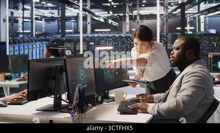 Server room manager supervise technician examining deep learning algorithms. Data center team leader and African american employee review performance dashboards of AI equipment rigs, camera A Stock Photo