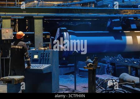 Factory engineer operates pipe painting automatic machine. Stock Photo