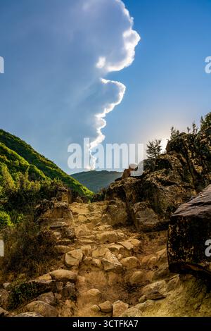 Rocky mountain path leading to Kabashi Waterfall in Albania under dramatic clouds and golden sunlight on a vibrant summer afternoon Stock Photo