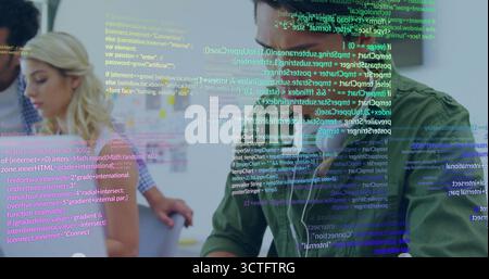 Coding developer wearing green shirt and earbuds at tech office desk, with laptop notes, copy space Stock Photo