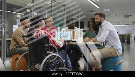 Coworkers collaborating around round table in open-plan office, with laptop charts and wheelchair Stock Photo