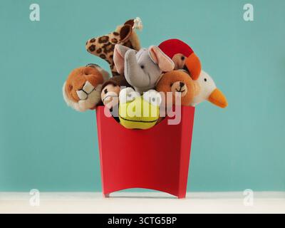 Group of cute animal finger puppets, including a lion, elephant, frog, bear, giraffe, monkey, and bird are placed in a bright red cardboard container Stock Photo