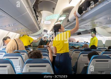 Cabin crew staff closing overhead carry-on luggage compartment inside Cebu Pacific Airbus A330neo aircraft. Stock Photo
