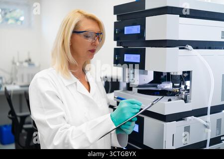 Laboratory worker taking notes during HPLC chromatography experiment in chemical research laboratory. Quality control concept. Stock Photo