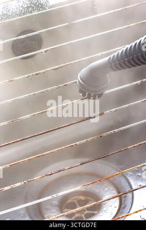 Steam cleaning grease off a stainless steel wire grill with a steam cleaner. Housework chore concept. Stock Photo
