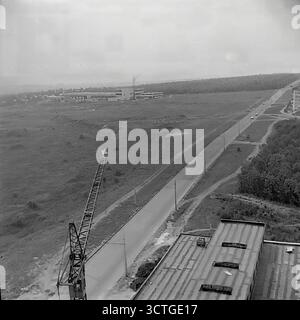 A panoramic view of urban expansion on the outskirts of the Artema microdistrict in 1970s Sloviansk, Ukrainian SSR. The photograph captures a newly constructed road stretching into the vast, undeveloped landscape. In the distance, the city's Bread Factory is visible. A construction crane in the foreground indicates that development of the area is still active. This image is a powerful symbol of the Soviet era's ambitious city planning and infrastructure projects, showing the city pushing its boundaries outwards to connect new residential and industrial zones Stock Photo