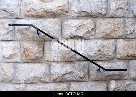 Iron Railing on Textured Stone Wall Surface. High quality photoSimple black iron handrail mounted on a rugged light beige stone wall. Clean architectural detail with texture and contrast,  Stock Photo