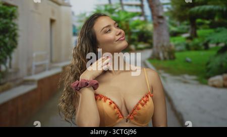 Woman smiling in orange bikini enjoying sunny day in green park with lush vegetation and cheerful outdoor vibes in summertime setting showing youthful Stock Photo