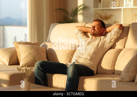 Happy man relaxing sitting on a comfortable couch at sunset at home Stock Photo