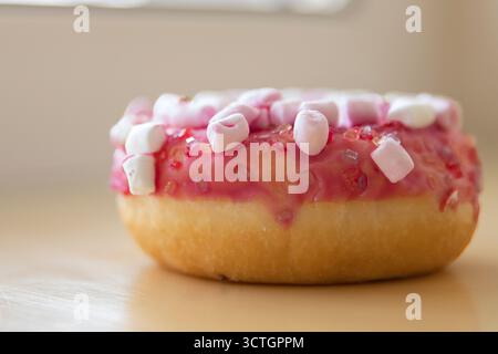 Pink donut with marshmallows and sugar icing on beige background. Sweet dessert with pink glaze and sugar pieces. Stock Photo