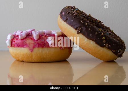 Two donuts with pink and chocolate icing on light background. Sweet dessert with sugar and cocoa glaze. Stock Photo