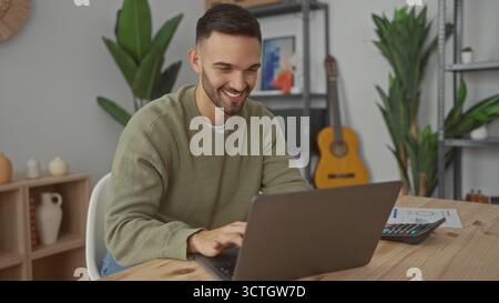 Young man working from home on a laptop in a cozy living room featuring plants and a guitar, focusing on a financial spreadsheet with a calculator nea Stock Photo