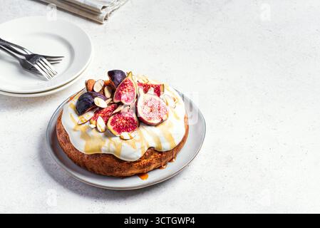 Honey sponge cake with whipped cream, figs and almond on white background, copy space. Homemade seasonal autumn cake with fruits and nuts. Stock Photo