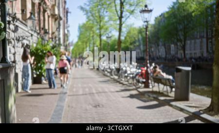 Blurred image of a vibrant amsterdam canal scene with people walking and cycling on a sunny day, capturing the essence of urban life in the netherland Stock Photo