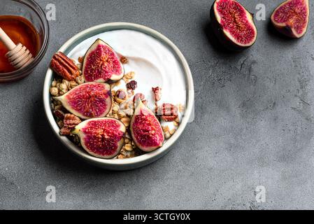 Granola bowl with figs and pecan nuts on gray concrete background, top view, copy space. Breakfast bowl with  yogurt, granola, honey, fruits and nuts. Stock Photo