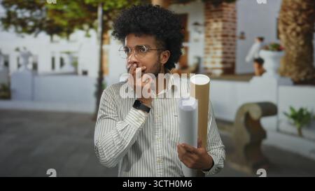 African american man holding blueprints on city street checks time looking at smartwatch. Stock Photo