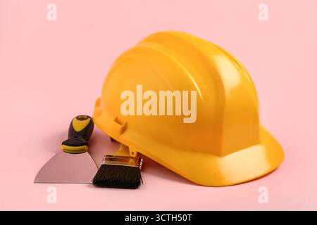 Hardhat with brush and putty knife on pink background, closeup Stock Photo