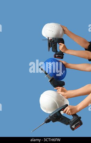 Hands with hardhats and construction tools on blue background Stock Photo