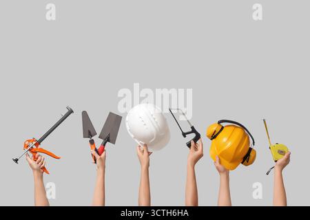 Hands with hardhats and construction tools on grey background Stock Photo
