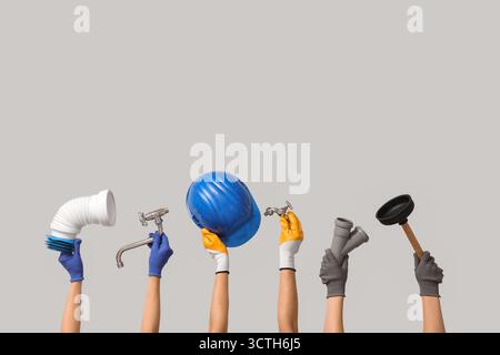Hands with hardhat and plumber supplies on grey background Stock Photo