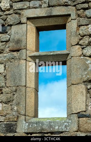 A weathered stone wall features a simple rectangular window. Through the opening, a cloudy blue sky is visible, adding a serene backdrop to the ancien Stock Photo