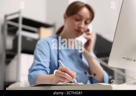 Nurse talking on telephone and taking notes at desk in office, selective focus Stock Photo