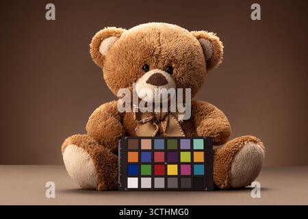 Soft plush brown teddy bear toy for kids with colorchecker color checker board or colours chart for calibrate, brown background Stock Photo