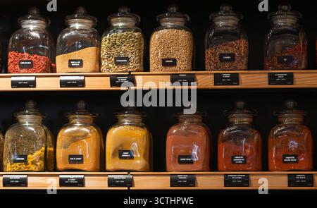 Various colorful spices and herbs displayed in glass jars on wooden shelves for bulk purchase in a retail store Stock Photo