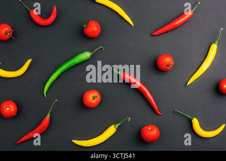 Colorful chili peppers and fresh tomatoes arranged on dark background, top view. Spicy food and healthy eating concept. Pattern, flat lay. Stock Photo