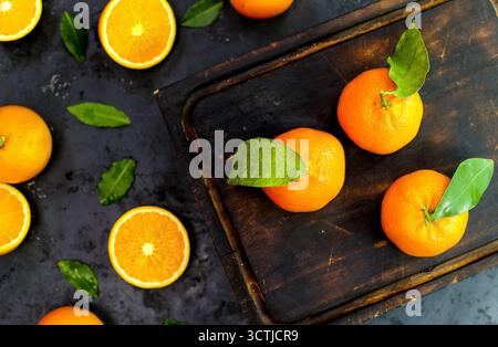 Horizontal composition of fresh oranges, some halved and some whole with leaves, photographed on a dark background in natural light. Stock Photo