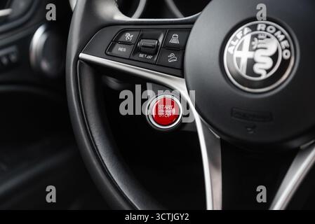 Alfa Romeo steering wheel with red start engine button and cruise control switches. Modern luxury car interior with black leather and metal trim. Stock Photo