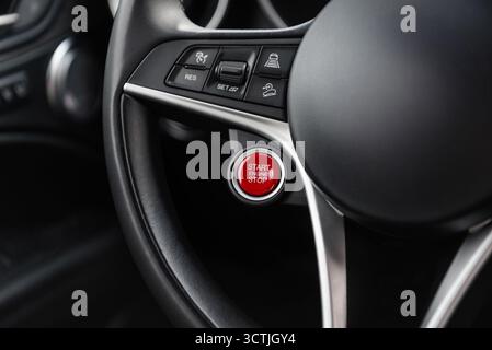 Car steering wheel with big red start engine button. Modern luxury car interior with metal trim Stock Photo