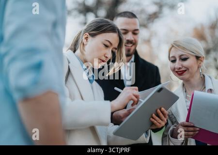 Colleagues collaborating on a project outdoors using digital devices and documents. Stock Photo