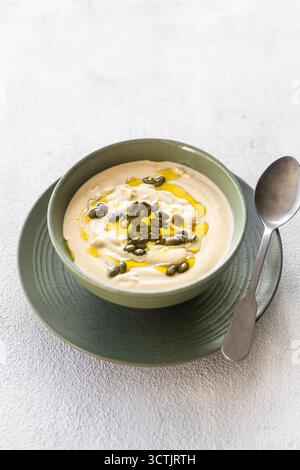 Smooth celery soup garnished with olive oil and pumpkin seeds, photographed in soft natural light on a light textured background for wellness themes. Stock Photo