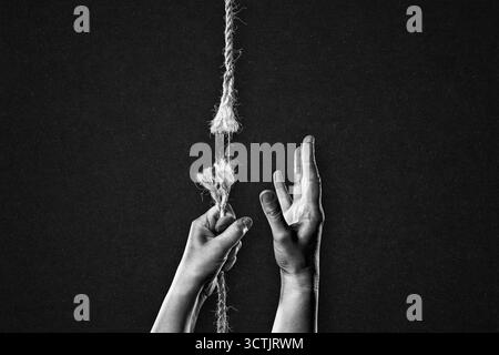 Hold on to Frayed Rope About to Break Asking for Help Against Textured Black Background Stock Photo